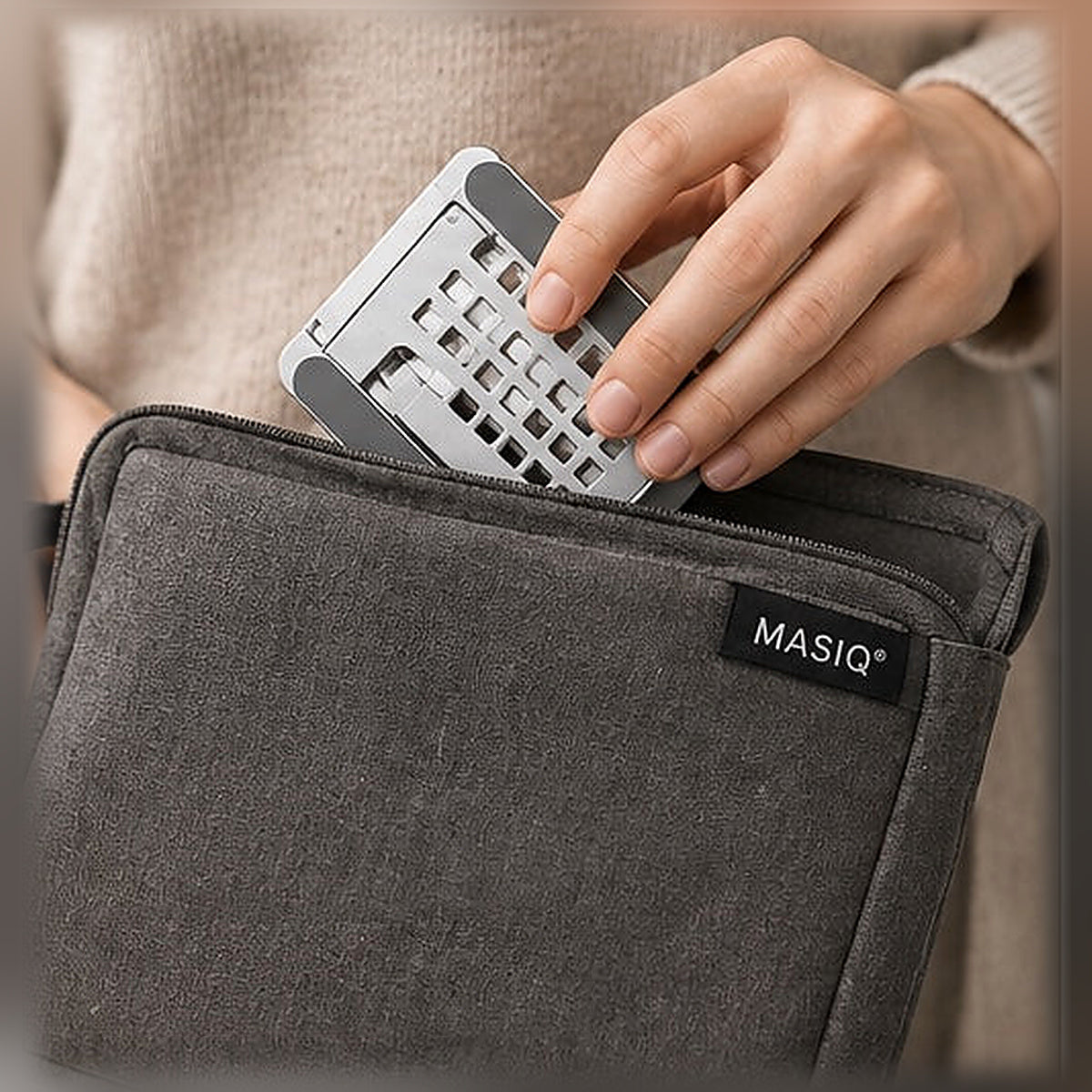 Een hand schuift de ingeklapte MASIQ tabletstandaard in een laptophoes
